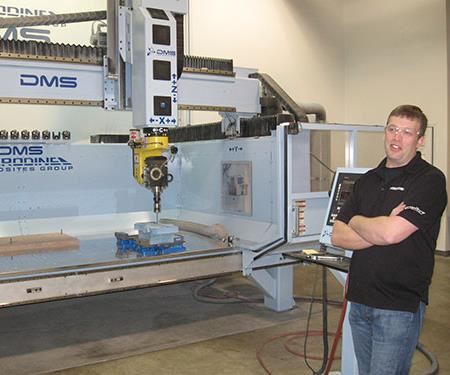 Kyle Castor stands in front of a five-axis router with arms crossed.