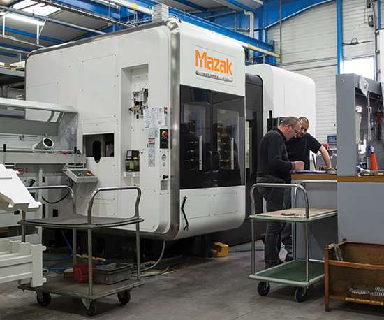 Two employees working at a workstation in front of a large machine tool.
