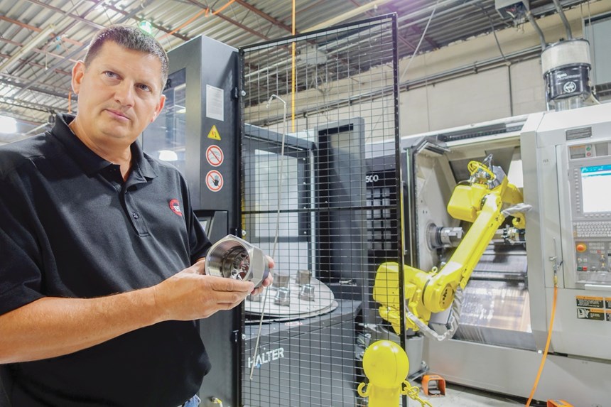 John Hicks holds a part in front of a robot cell