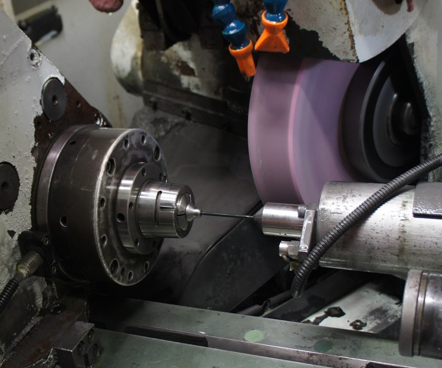 Grinding wheel and fixturing are visible in the workzone of a machine set up to grind between centers, a process that is generally more complicated than centerless grinding. 