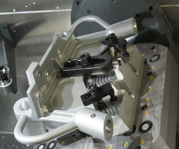 A five-axis table tilts to provide spindle access to bores on a part held in a custom workholding fixture. 