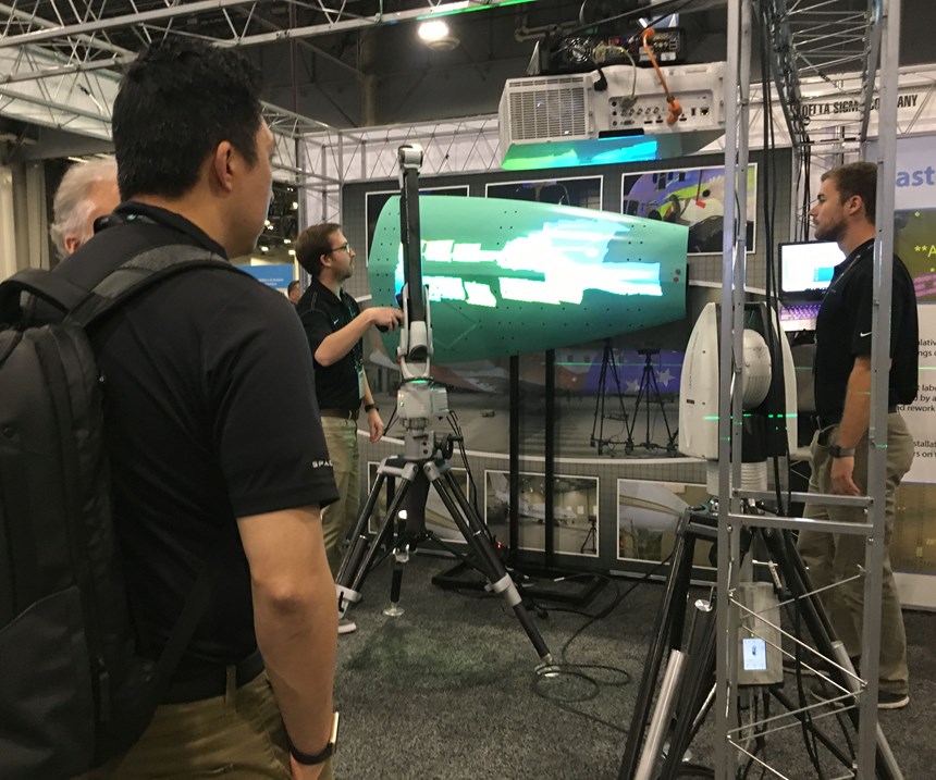 A HxGN Live 2018, attendees look on as a company representative uses a scanner to capture the geometry of a large aircraft wing structure. 