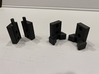 Two parts of a 3D-printed custom robot gripper for tending CNC machining centers are laid out on the table at Advanced Precision Engineering (APE).