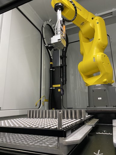 A robot arm manipulates cylindrical tool bodies inside a laser marking machine. 