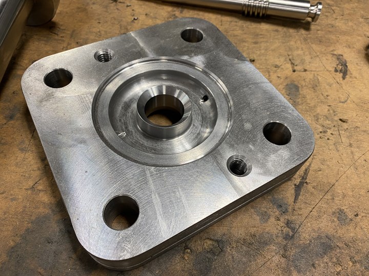 A flat, square metal part produced by at Kustom Machining & Manufacturing in Jackson, TN. features numerous large bores. 