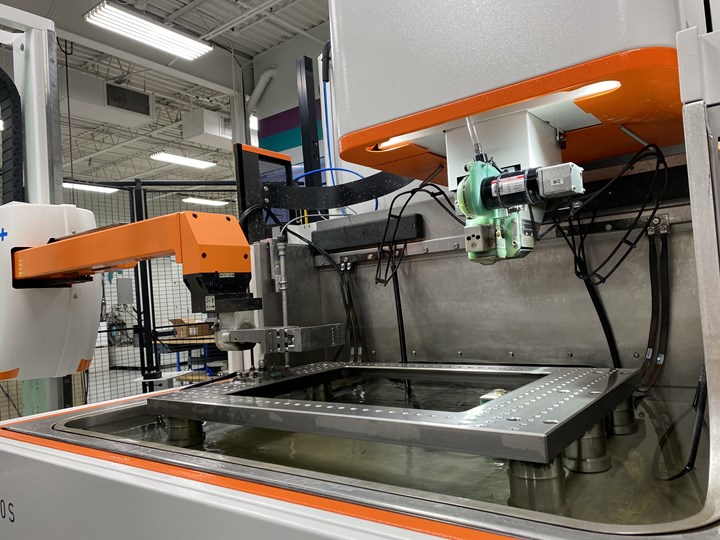 A robot arm reaches into the workzone of an EDM. 