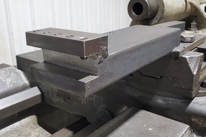A large, rectangular toolholder in the foreground helps clear the cross slide on the manually operated turning machine visible in the background.
