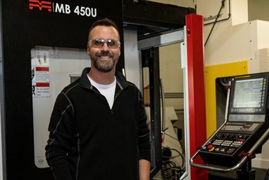 A photo of Evan Jones, 3rd Gen Machine founder, in front of the controls of a Methods 450U. The JobShop Cell is on the other side of the control panel.