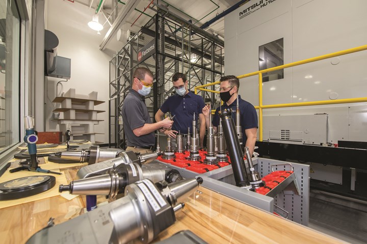Ryan Patry, manufacturing engineer, Pete Germanowski, chief engineer and Jason Pratts, manufacturing engineer, all in masks, huddle around a table to review cutting tools in the CNC machining cell at Sikorsky’s digital factory. 