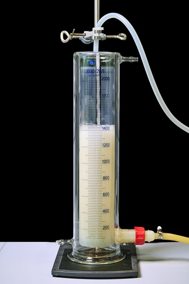 Image of glass beaker tube of white opaque liquid with  a series of tubes being inserted for testing