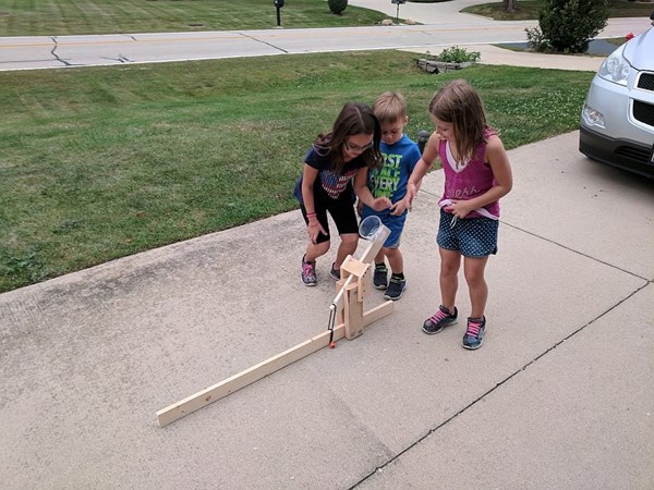 Kids playing with a catapult they built with their dad to learn how to make something.
