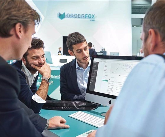 Four people standing around monitor with Orderfox marketplace on the screen