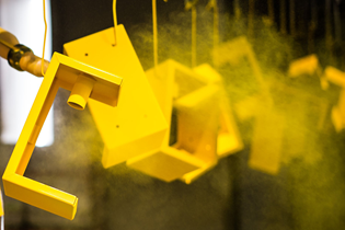 metal part with yellow powder coating hanging on a rack after being sprayed
