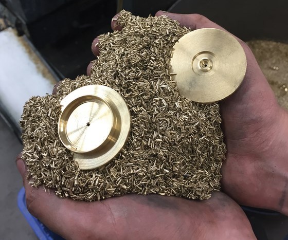 hands holding a pile of tiny brass machined parts as well as two large circular parts