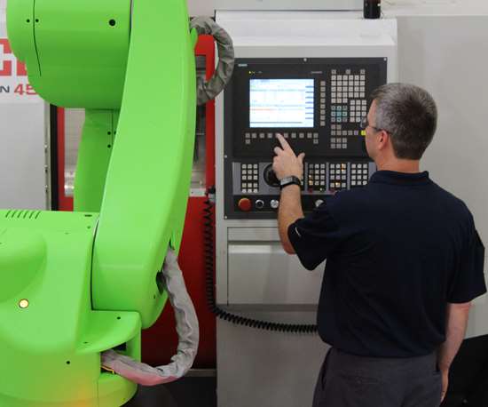 An employee stands next to a cobot at a machine tool