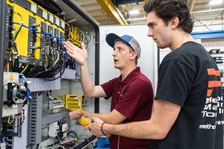 two workers looking at the internal wiring of a machine to test for errors