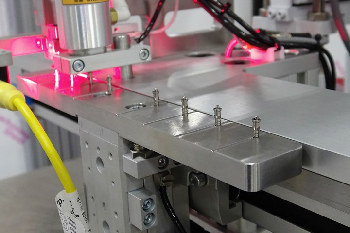 Micro-inserts loaded on pins on a shuttle prior to pickup by a robot. Red light is flash illumination for camera inspection.