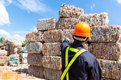 worker looks at a large pile of baled plastics