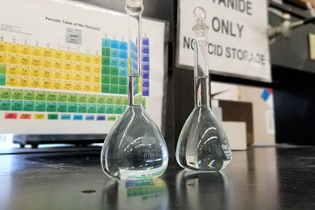 periodic table in background with two beakers on the table in front