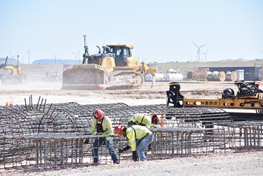 Image of construction workers moving and adjusting rebar  on job site with large equipment in the background, moving across a wide open construction site.