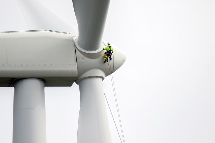 Rope access technicians rappelling down to working on blade of wind turbine.