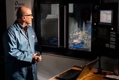 An image of a man watching over a machining operation, with a large coolant spray inside the machine