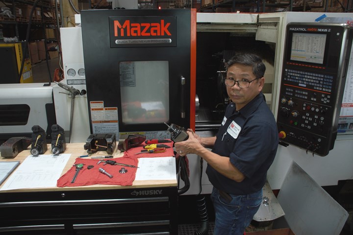 A photo of Trak machine operator Tim holding a live tooling fixture and standing in front of a Mazak mill-turn