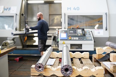 A photo of a Wittmann Battenfeld employee handling a workpiece on the M40 mill-turn. Two workpieces with wave-shaped exteriors rest on a stand in the foreground.