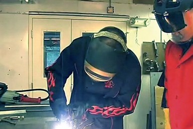 A photo of a student working with a plasma cutter while a teacher watches