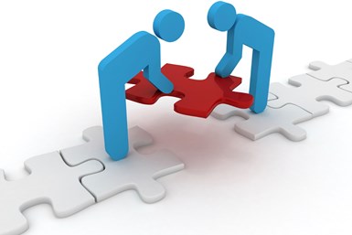 A stock photo of two stick figures standing on white puzzle pieces, fitting a red puzzle piece into the space between them