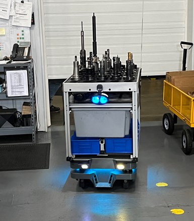 A photo of an autonomously driving tool cart. Blue headlights on the front give it a slightly bug-eyed appearance.