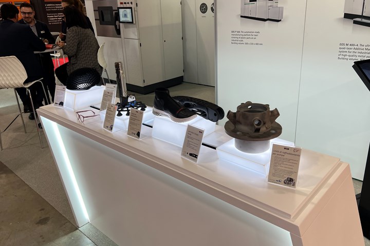 A photo of products made with additively manufactured parts produced on EOS printers, as seen at BI-MU 2022. the products include shoe soles, glasses frames, an airplane arm rest and more.