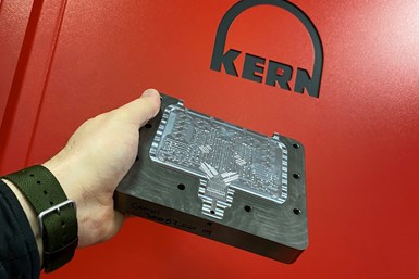 A photo of a person holding a microfluidics mold in front of one of the Kern machines. The Kern logo is visible on the machine.