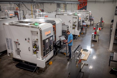 A photo of multiple, identical Mazak Integrex Multi-Tasking machines on a shop floor, with a shop employee working with the controls of one machine.