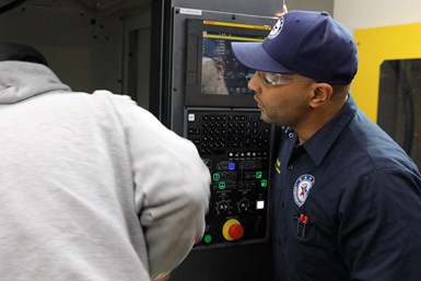 A WFW instructor watches a trainee working on a CNC machine