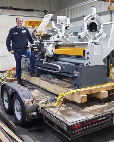 Josh Topper stands on a tractor-trailer in his garage aside his brand new manual engine lathe.