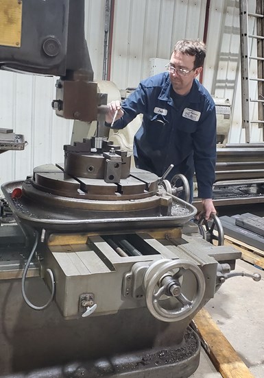 Josh Topper manipulates the handwheels of a vertical slotting machine. 