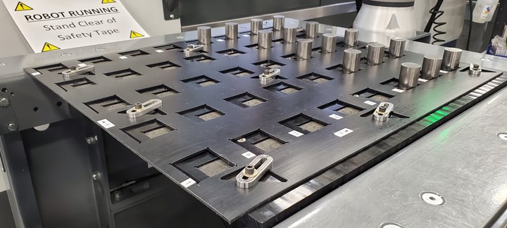 A system of overlapping trays features adjustable square openings that stage multiple, metal workpieces for pickup and loading into a CNC machine tool with a robot arm. 