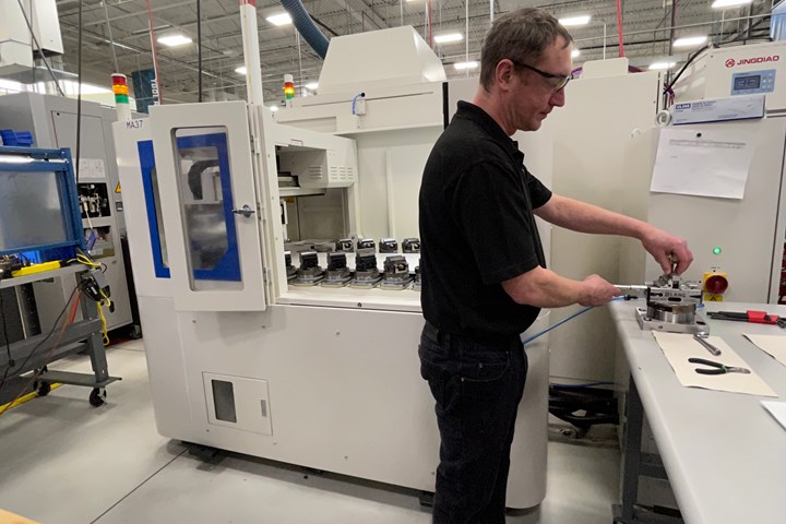 A machinist at Metal Craft fixtures a part to a pallet in front of a five-axis machining center pallet changer. 