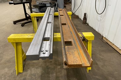 Two track rails next to each other on trestle-tables. The one on the left is the new, machined version, while the one on the right is the welded original.
