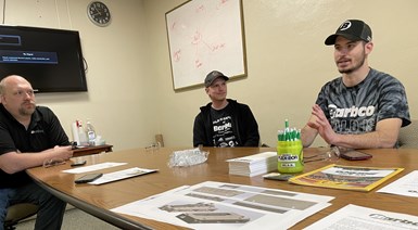 A photo of three Barbco employees at a table. One is talking while the other two listen.