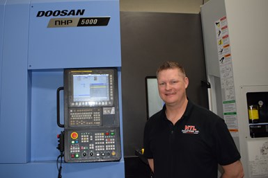 A photo of Greg McArthur standing in front of a DN Solutions NHP5000