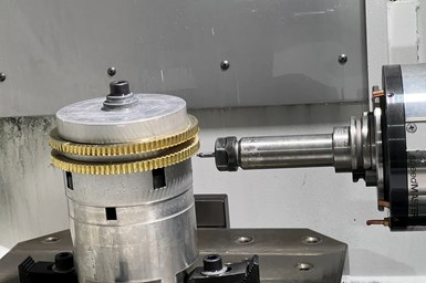 Two wheels mounted on a horizontal machining center's worktable. A milling tool waits just below the wheels' teeth.