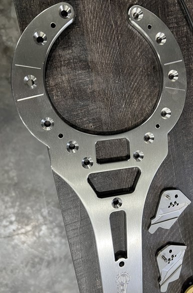 A wrench-shaped aluminum part with small holes interspersed among the countersinks. An engraving is just visible at the bottom.