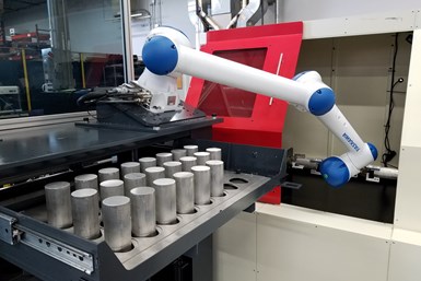 A photo of a machine-tending robot reaching into a machine with a round bar