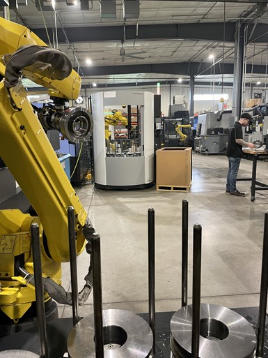 A robot loads parts on the left, while a shopfloor employee performs an inspection task to the right.