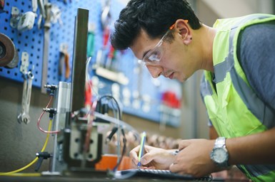 A person writing something down in a machine shop environment.