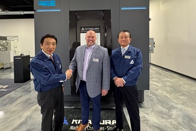 People shaking hands in front of a machining center.