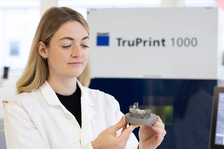 TruPrint 1000 system in the background, with an engineer holding up a dental prosthetic.