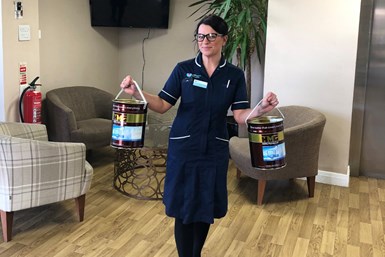 A photo of a hospice worker posing with two paint buckets filled with HMG hand sanitizer